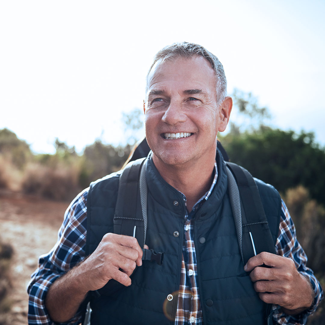 older male adult with a backpack on hiking in nature \ article on how advancements in cellular health can help with healthy aging