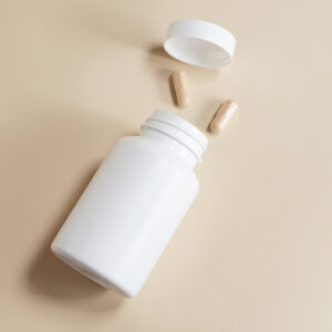 white pill bottle with tan background and two tan/brown capsules coming out of the pill bottle
