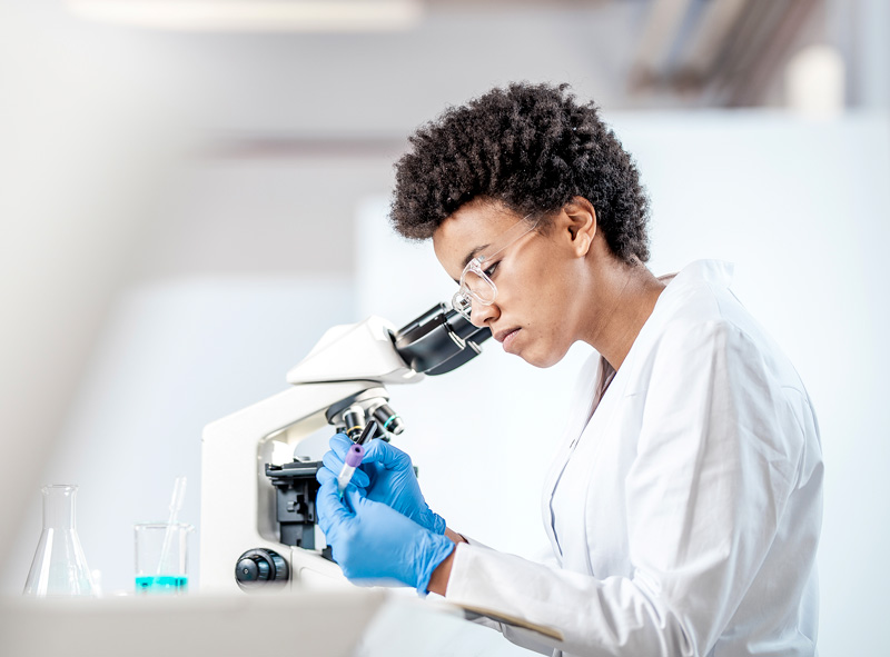 science lab with a woman in a white lab coat looking through a mircoscope
